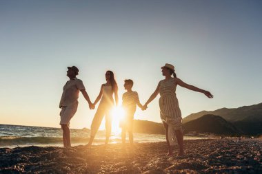 Anne, baba ve çocuklar kumsalda gün batımının tadını çıkarıyorlar. Mutlu aile seyahatleri ve tatil konsepti.