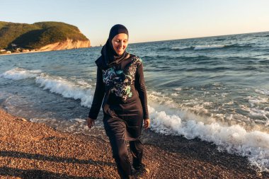 Sahilde durup ufka bakan tesettürlü bir kadın.