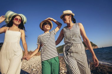 Anne ve çocuklar kumsalda gün batımının tadını çıkarıyorlar. Mutlu aile seyahatleri ve tatil konsepti.