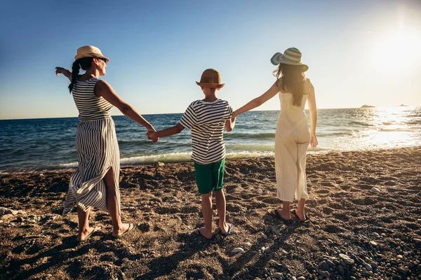 Anne ve çocuklar kumsalda gün batımının tadını çıkarıyorlar. Mutlu aile seyahatleri ve tatil konsepti.