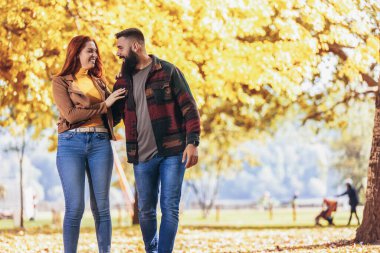Genç mutlu çift el ele tutuşup sonbahar parkında yürürken birbirlerine bakıyorlar..