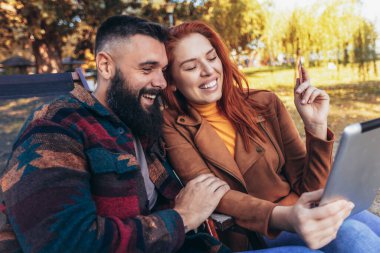 Güzel bir çift bir kafede oturmuş limonata içip sohbet ederken kredi kartı ve dijital tabletle online alışveriş yapıyorlar..