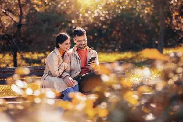 Młoda Para Spogląda Tablet Siedzą Ławce Słoneczny Jesienny Dzień Kolorowym — Zdjęcie stockowe