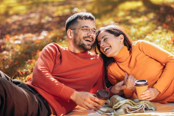 在一个阳光明媚的秋日 这对年轻夫妇手牵手躺在公园里喝咖啡 — 图库照片
