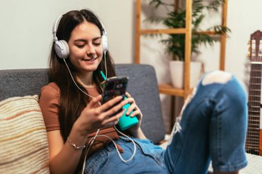 Beautiful teenager girl surfing social media on smart phone while having leisure time at her home.