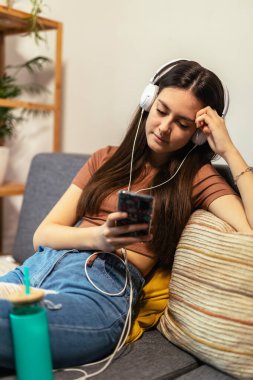 Beautiful teenager girl surfing social media on smart phone while having leisure time at her home.