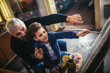 Baba ve oğul resim stüdyosunda birlikte çalışıp resim yapıyorlar.
