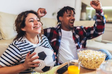 Afrikalı Amerikalı koca ve Latin kadın evlerinin rahatlığından televizyonda futbol maçı izliyorlar..