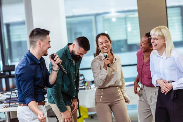 Group of professional people singing karaoke in the modern office
