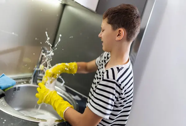 Child washing the dishes in the sink and having fun