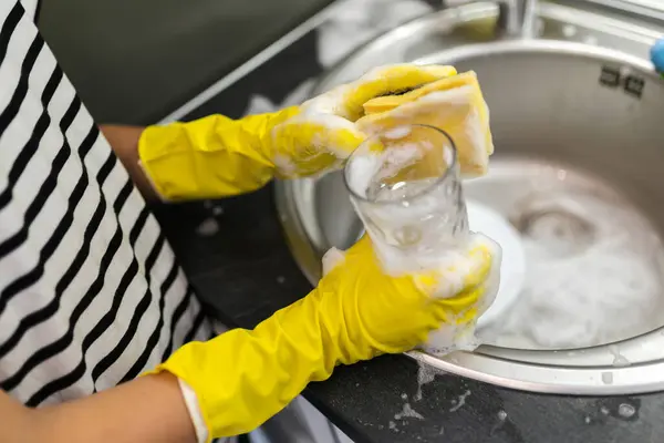 Close-up of hands washing the dishes in the sink.