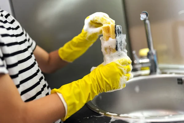 Close-up of hands washing the dishes in the sink.