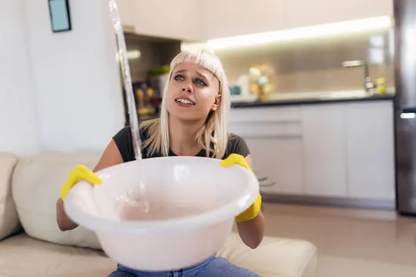 Young blonde woman is holding a bowl because her roof is leaking