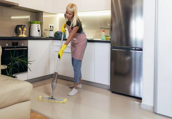 Young blonde woman cleaning a kitchen floor