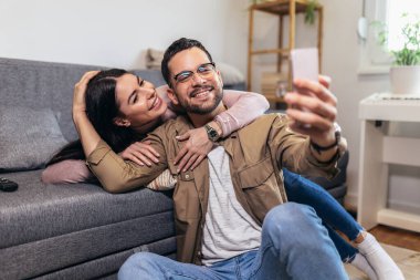 Beautiful young loving couple bonding to each other and making selfie while sitting on the couch together
