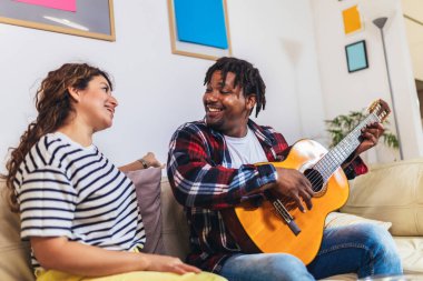 Mutlu genç çift evdeki kanepede gitar çalarak şarkı söylüyor.