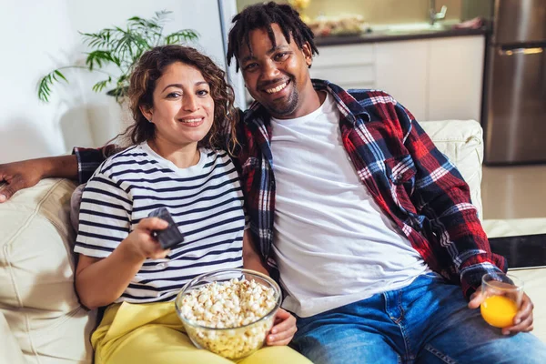 Young happy couple watching movie on TV and eating popcorn while relaxing in the living room.