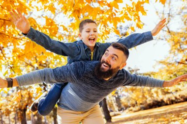 Baba sırtında bir oğul taşıyor. Güneşli bir sonbahar gününde renkli parkta eğleniyorum..