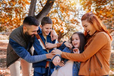 Parents tickle their children. Sunny autumn day in the colorful park clipart