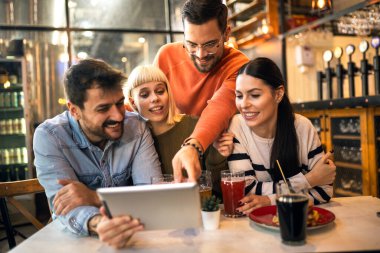 Kafede otururken dijital tablete bakan genç arkadaşlar. 