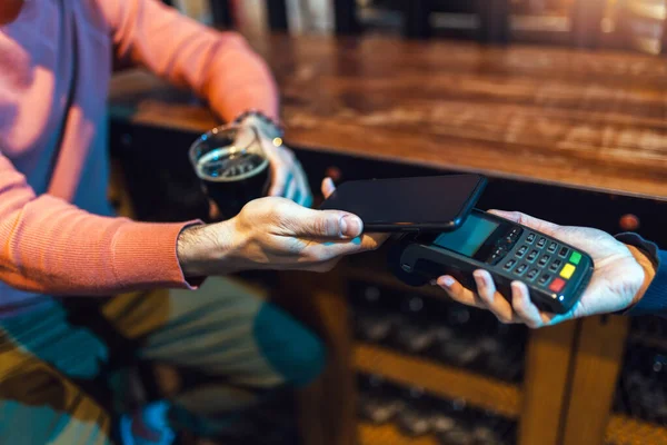 Man in bar paying with cellular device