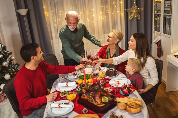 おじいさんはテーブルで乾杯しています 自家製の食べ物を食べながらクリスマスを祝う家族 — ストック写真