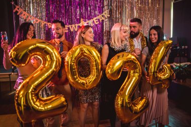 Yeni yılı gece kulübünde kutlayan bir grup genç. Altın numaralı balonları tutuyorlar.