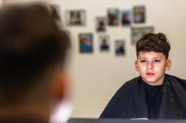 Shot of little kid covered with black cloth by hairdresser