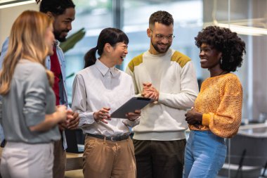 Çok ırklı meslektaşlar bir arada duruyor ve modern ofislerindeki iş hakkında konuşuyorlar..