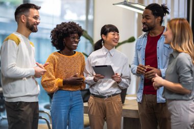 Çok ırklı meslektaşlar bir arada duruyor ve modern ofislerindeki iş hakkında konuşuyorlar..