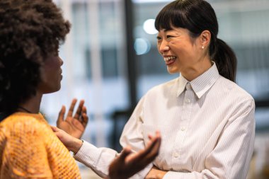 Çok ırklı meslektaşlar bir arada duruyor ve modern ofislerindeki iş hakkında konuşuyorlar..