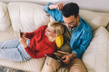 Kanepede sarılan, dijital tablet ve telefon kullanan güzel bir çift..
