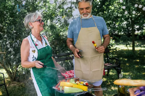 Elderly people are making barbeque, drinking beverages, making memories, and laughing.