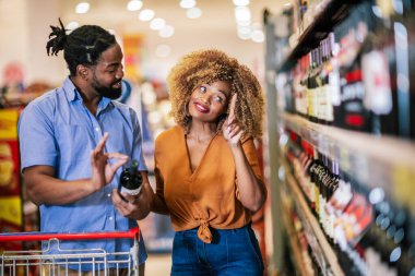 Alışveriş merkezinde market alışverişi yapan Afro-Amerikalı bir çift. Şarap alıyorum..