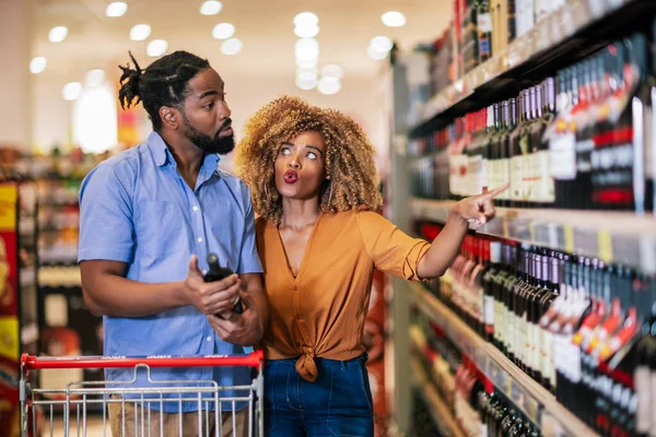 African American couple with trolley purchasing groceries at mall. Buying wine.