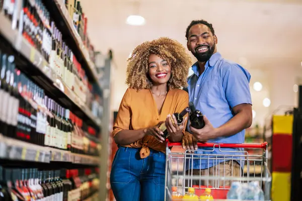 African American couple with trolley purchasing groceries at mall. Buying wine.