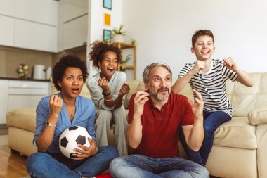 Heyecanlı aile futbolu hayranları birlikte maç izleyip golü kutluyorlar.