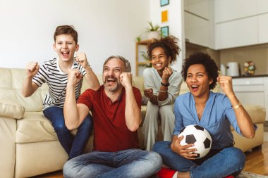 Heyecanlı aile futbolu hayranları birlikte maç izleyip golü kutluyorlar.