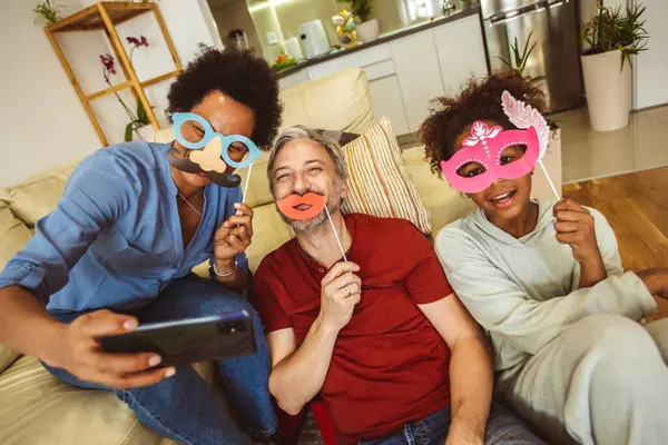 Happy family with party props taking selfie by smartphone sitting on sofa at home