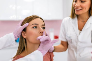 Estetik ameliyatlardan önce bir doktor hastayı muayene eder. Hasta kendine bakar ve neyi değiştirmek istediğini söyler..