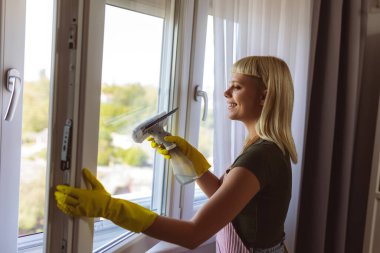Genç sarışın kadın evinin camlarını temizliyor.