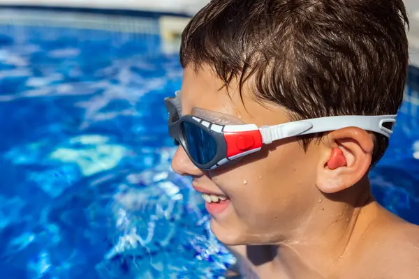小さな少年はプールで泳ぎ 耳栓とゴーグルを持っています 夏休みについて — ストック写真