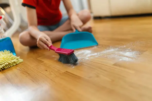Male child cleaning the dust of the floor. Doing his chores.