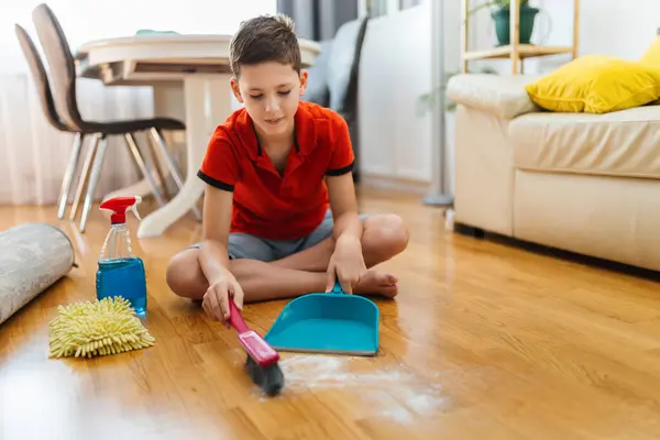 Male child cleaning the dust of the floor. Doing his chores.