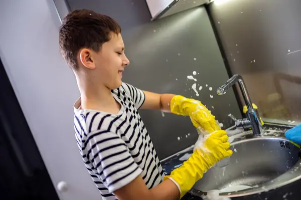 Child washing the dishes in the sink and having fun