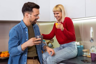 Genç bir adam ve kadın mutfakta dikilip konuşuyorlar. Mutfakta kahve ve meyve suyuyla duran mutlu eş ve koca..