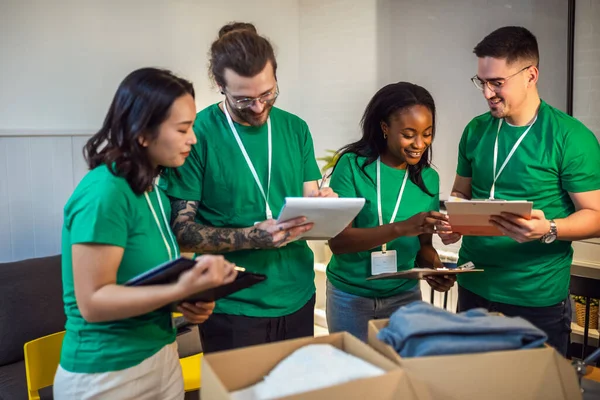 Smiling activists putting second-hand clothes in cardboard boxes for donation.