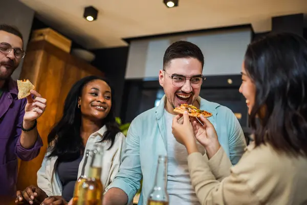 Multi-ethnic friends with pizza and bottles of drinks having party