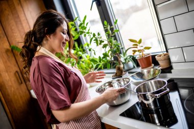 Latin kadın modern mutfağında yemek pişiriyor tencerede karıştırıyor akşam yemeği hazırlıyor.. 