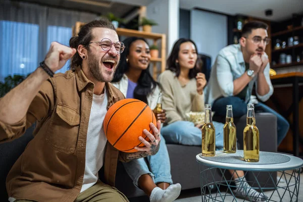 Multiracial group of friends watching basketball game, drinking beer and cheering.